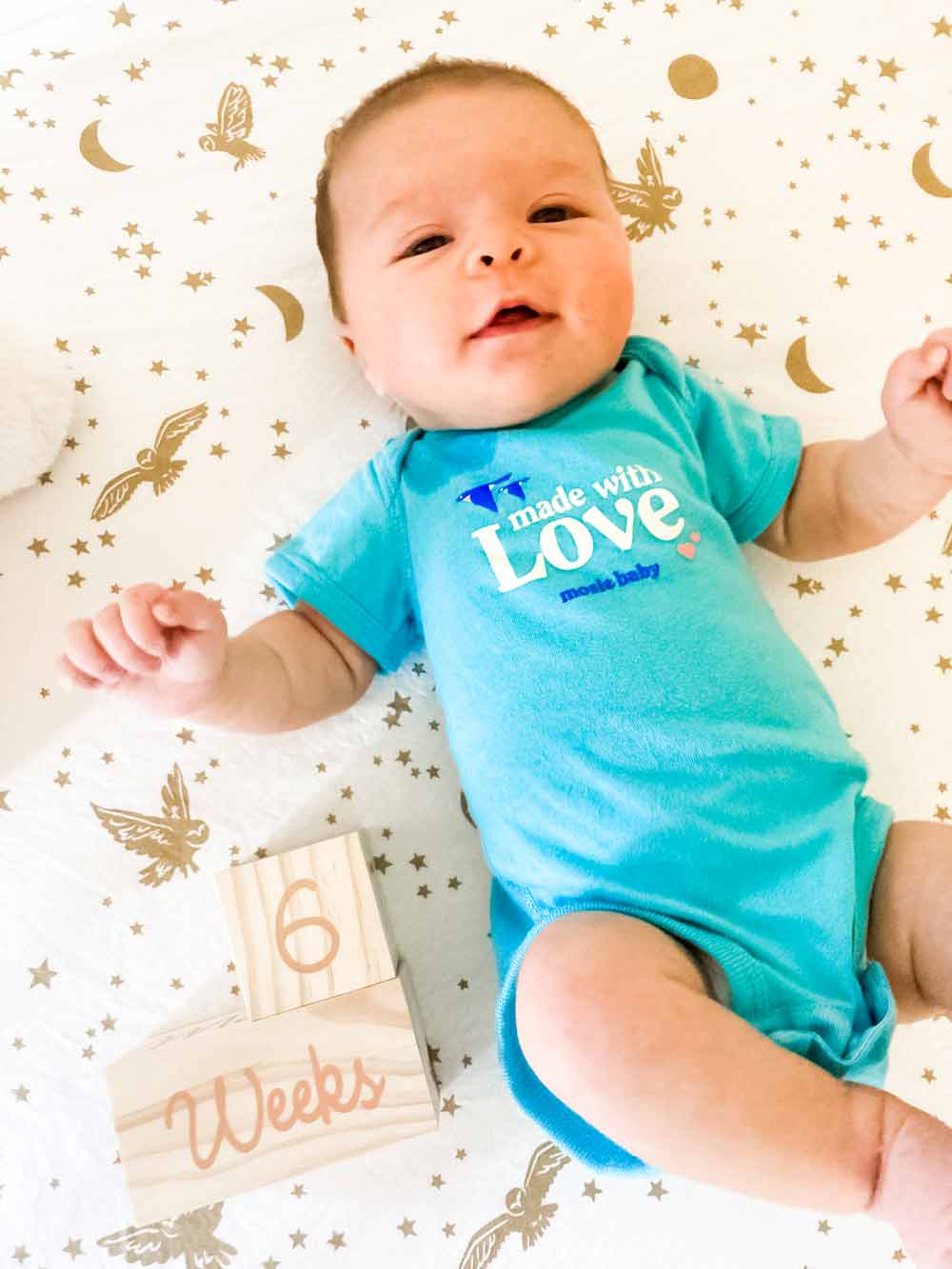 Mosie baby lays in Mosie baby onesie next to 6 weeks milestone announcement in wooden blocks.