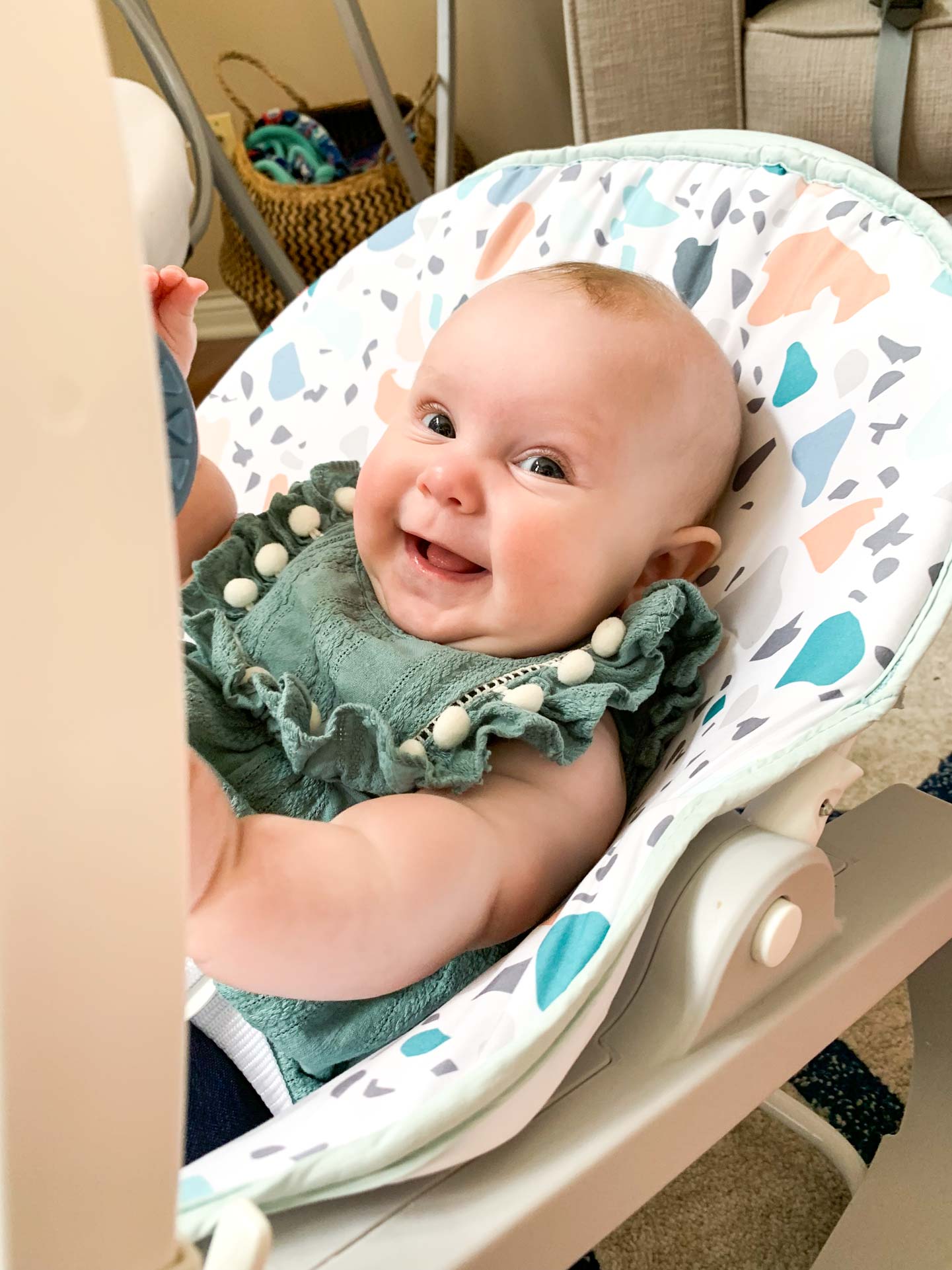 Mosie Baby smiles and lays in baby chair in green onesie