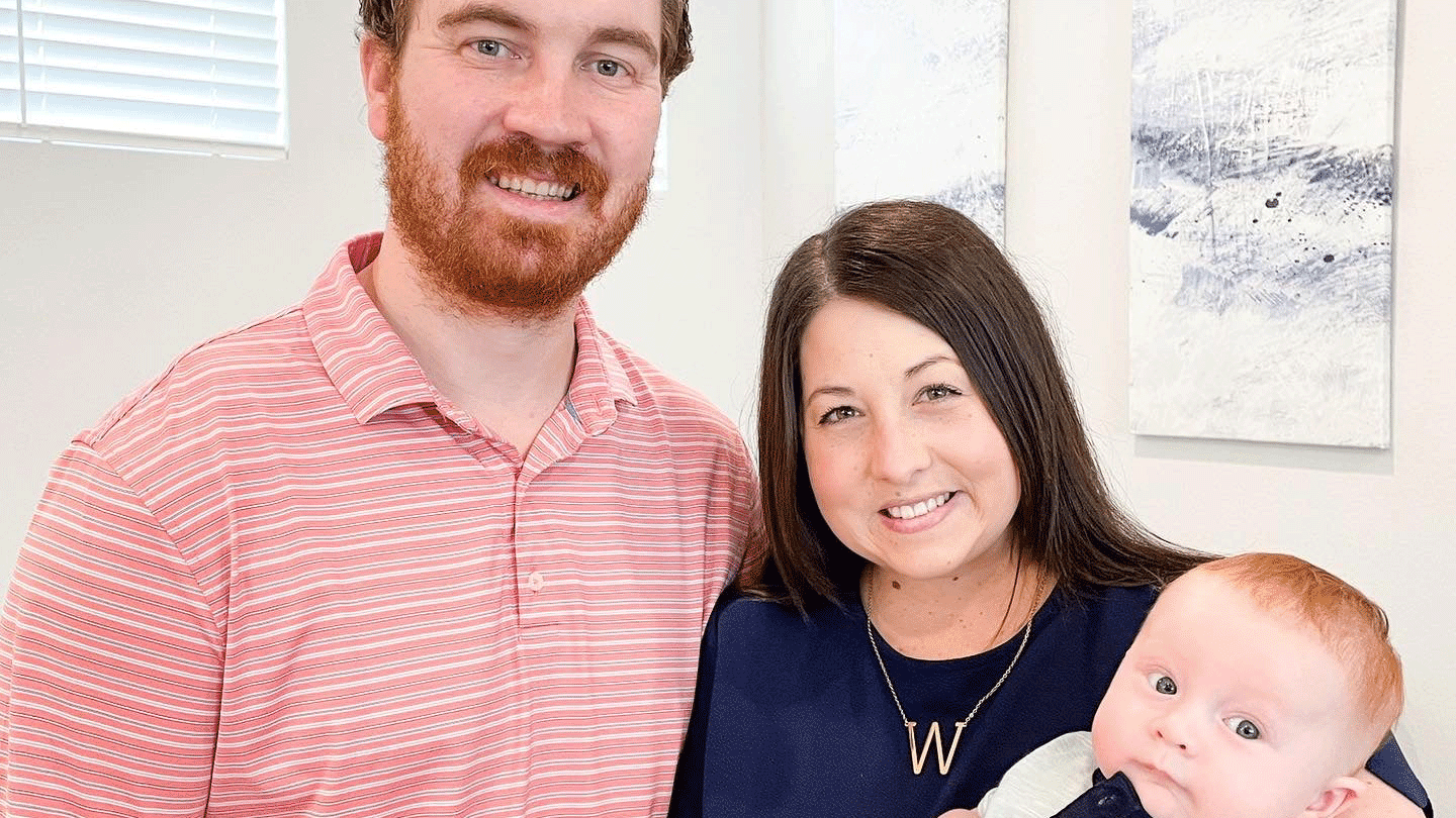 A man and woman stand holding their newborn