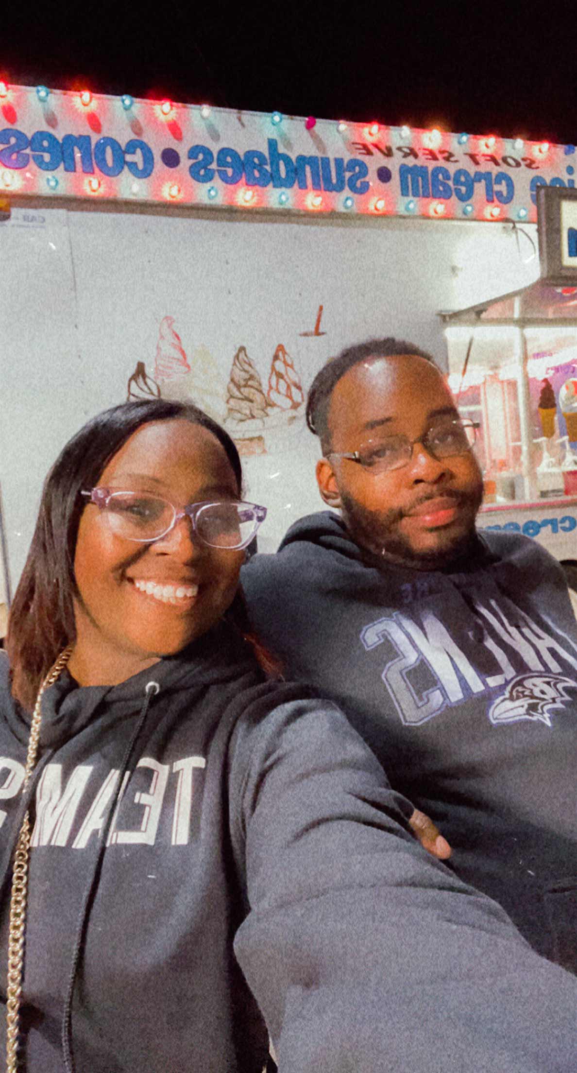 Heterosexual couple smiles into camera with gray hoodies at Carnival