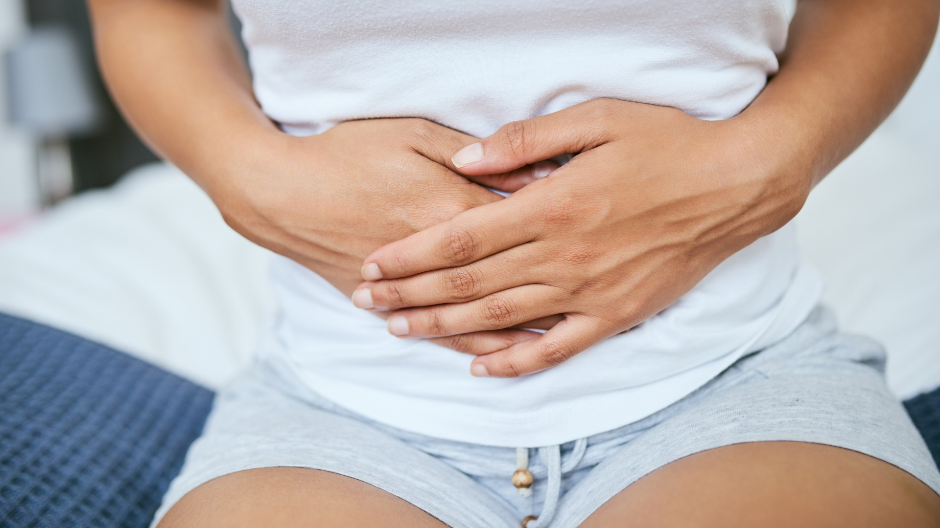 Woman lies on couch in abdomen pain in striped long sleeve shirt, jeans and socks in her home