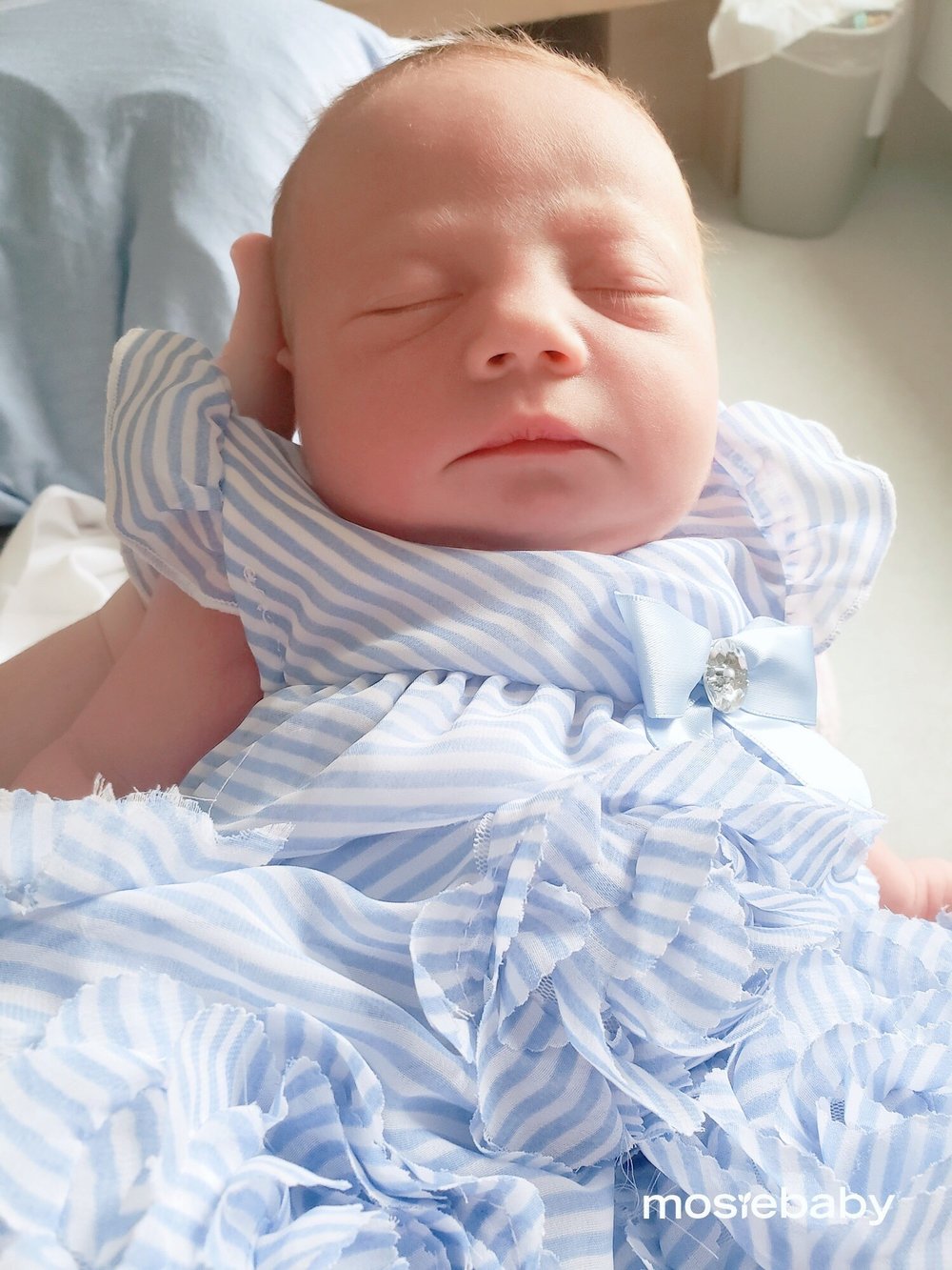 A sleeping newborn Mosie Baby in a blue dress